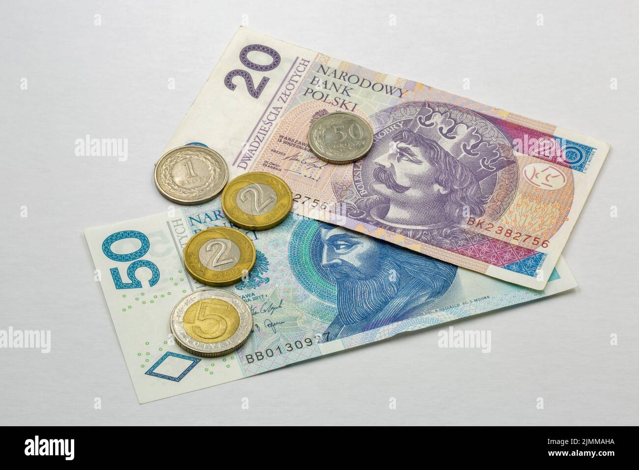 Banconote e monete polacche a venticinque zloty si accavallano contro il bianco Foto Stock