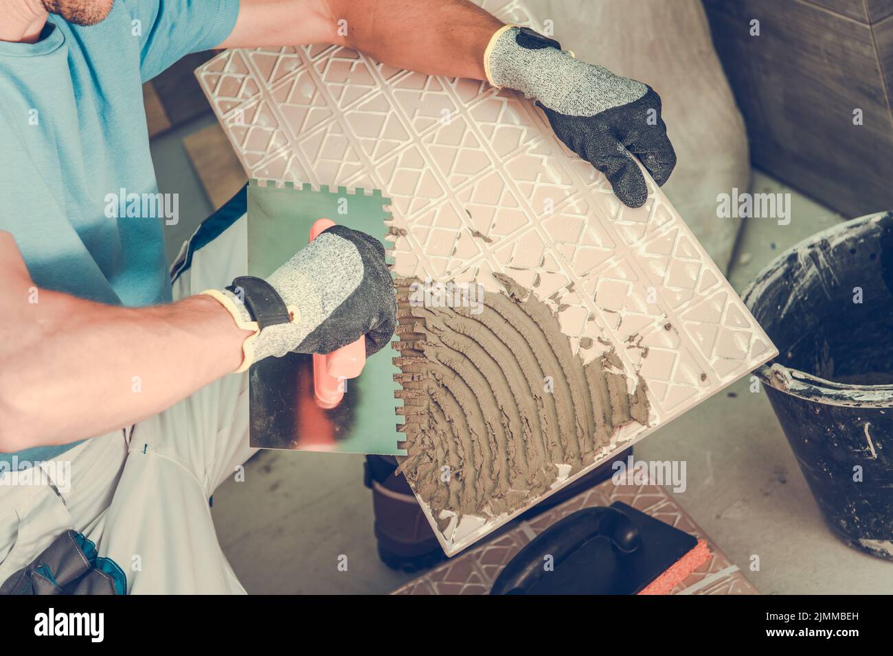 Primo piano di adesivo per piastrelle applicato alla piastrella da lavoratore maschio prima di installarla in bagno. Vista dettagliata. Tema del lavoro di ristrutturazione. Foto Stock