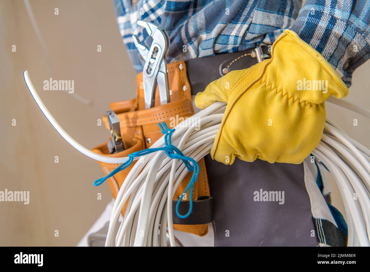 Primo piano dei cavi elettrici bianchi tenuti nella mano sinistra di un elettricista che indossa guanti protettivi gialli per costruzioni. Tema industriale. Foto Stock
