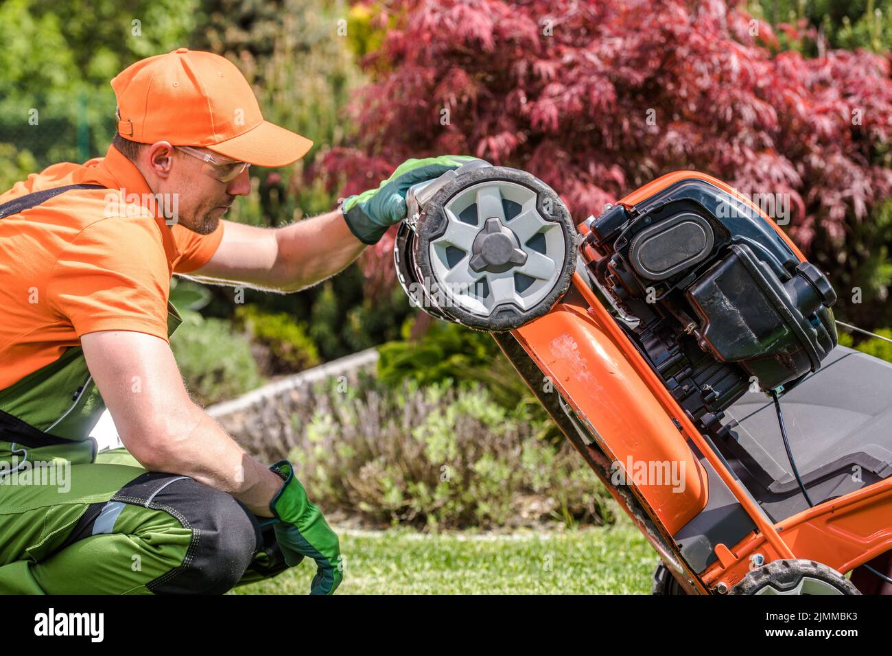 Primo piano di giardiniere maschio caucasico nel suo lavoro indossare attentamente controllo il suo professionista giardiniere strumento di potenza falciatrice prima di tagliare l'erba. Gar Foto Stock
