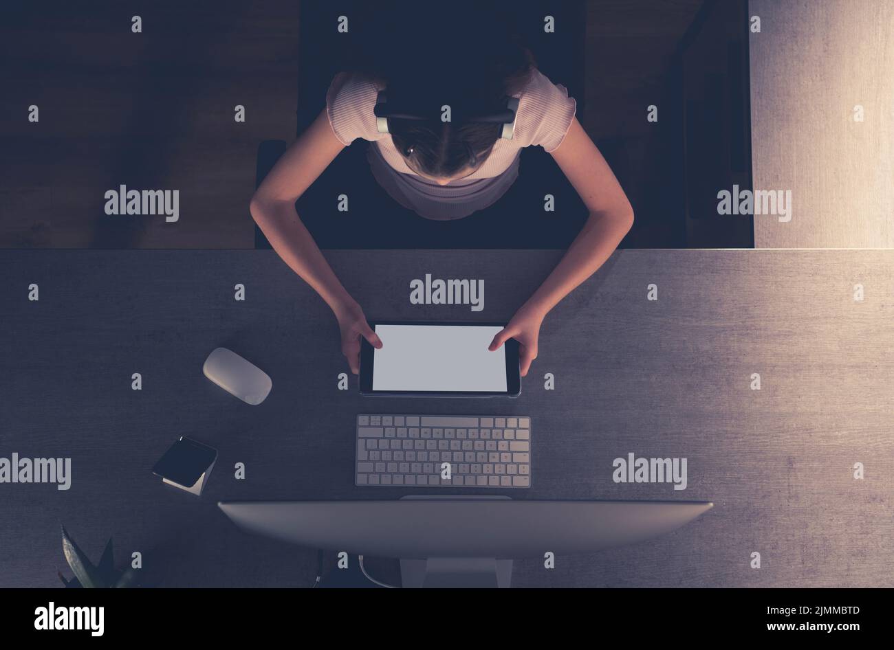 Vista aerea di una ragazza che naviga su Internet sul suo tablet seduto su una scrivania di fronte a un monitor di computer che studia per le sue classi scolastiche. Perfetto Foto Stock