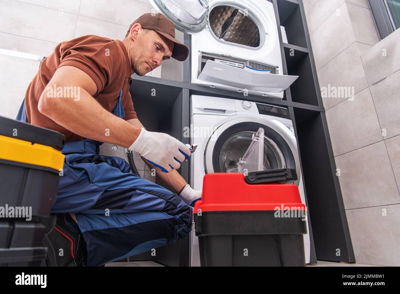 Lavoratore caucasico al suo 40s fissare e sbloccare la lavatrice nella lavanderia del suo cliente. Tema dei servizi professionali di riparazione della casa. Foto Stock