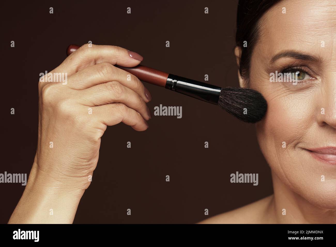 Donna di mezza età che applica polvere di fondazione o arrossamento sul suo viso Foto Stock