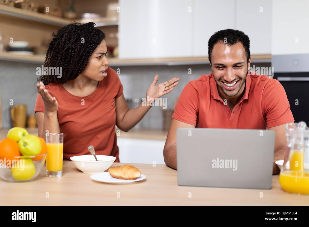 Delusa la giovane moglie afroamericana arrabbiata urlando per sorridere marito, ragazzo giocare al computer portatile Foto Stock
