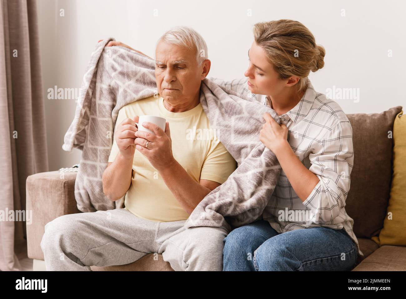 Giovane donna che si prende cura del nonno anziano con un sipto freddo a casa Foto Stock