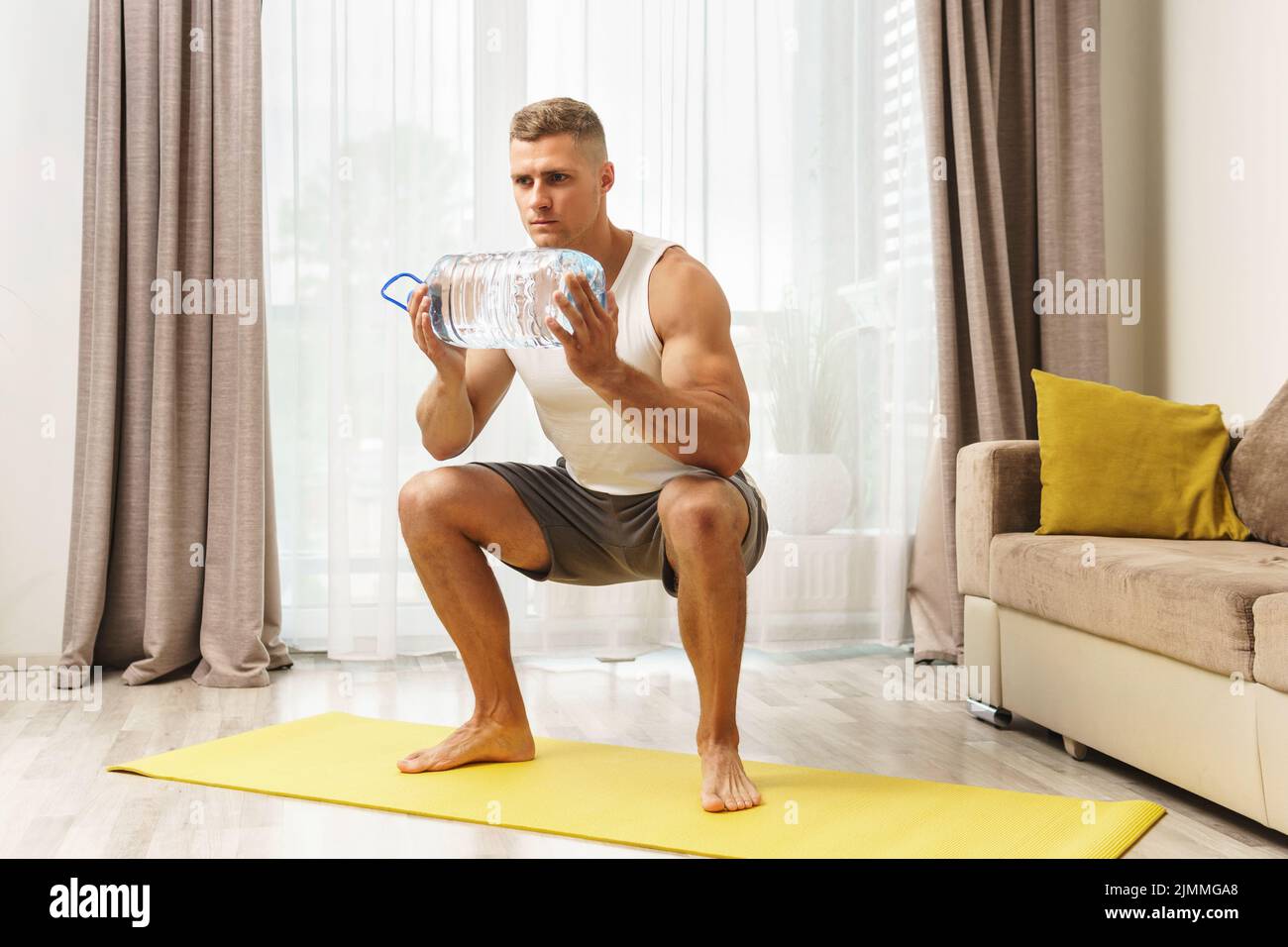 Giovane uomo atletico che usa una bottiglia grande di acqua per l'allenamento domestico Foto Stock