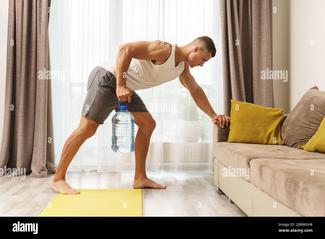 Giovane uomo atletico che usa una bottiglia grande di acqua per l'allenamento domestico Foto Stock