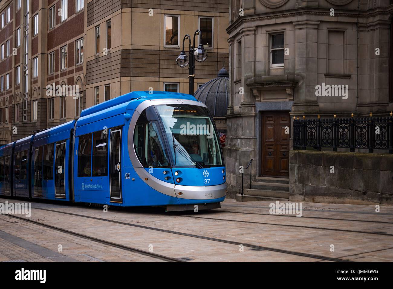 Birmingham, Regno Unito, moderno tram cittadino blu che attraversa il centro della città passando per i vecchi edifici. Foto Stock