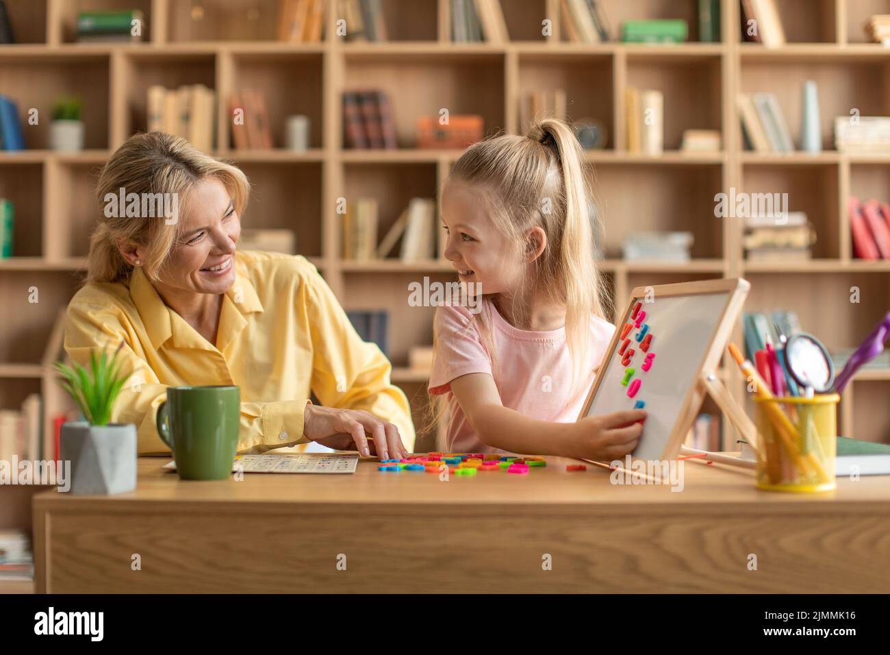 Istruzione prescolare. Insegnante professionista felice esercitandosi con la ragazza, bambino carino che legge le lettere e facendo le parole Foto Stock