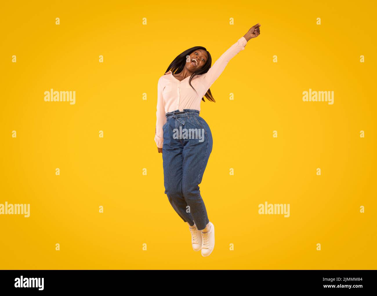 Gioiosa signora afroamericana che salta in aria e guarda la macchina fotografica, donna che si diverte su sfondo giallo studio Foto Stock