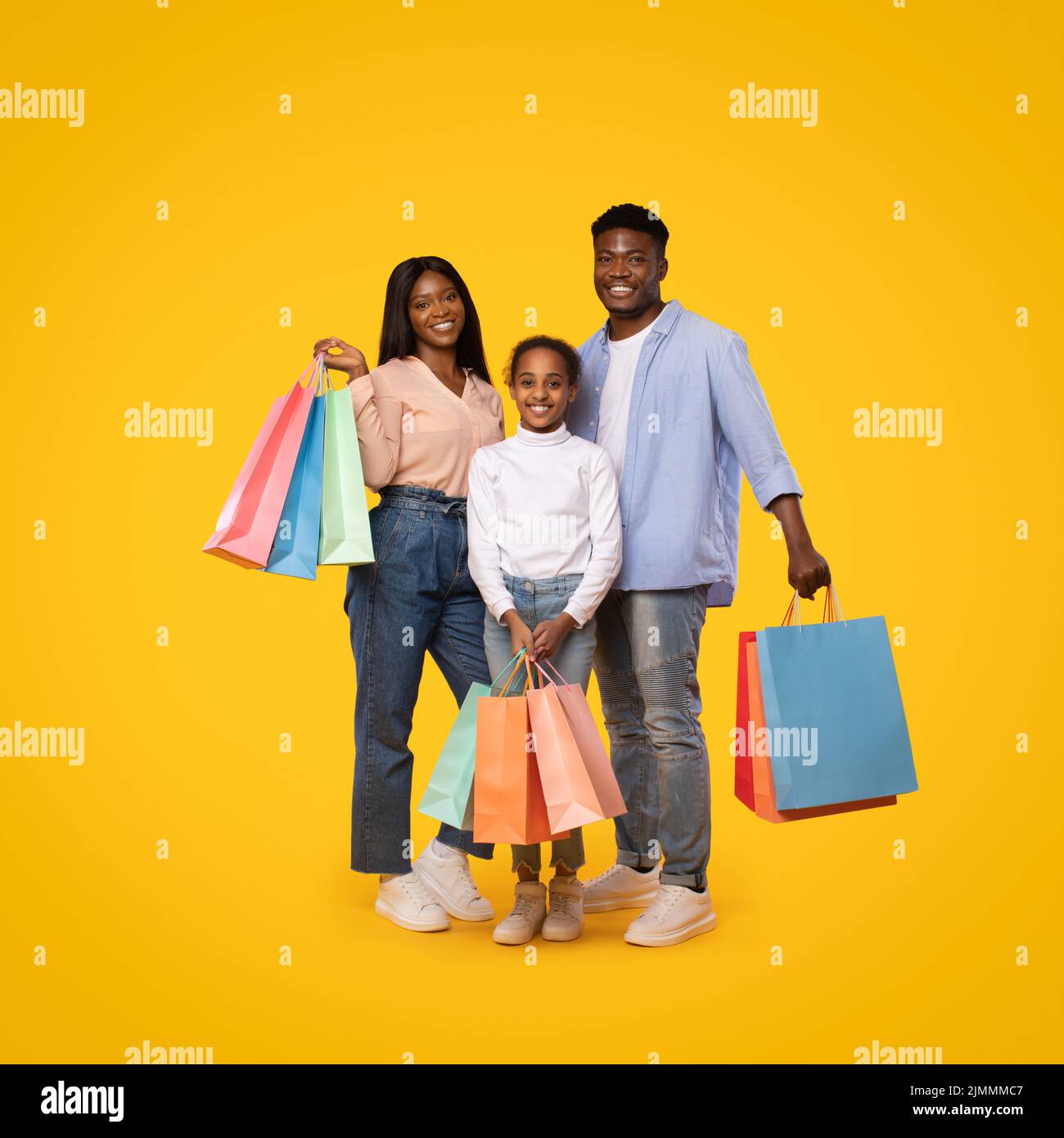 Concetto di vendita stagionale. Felice famiglia afroamericana di tre in posa con borse shopping su sfondo giallo Foto Stock