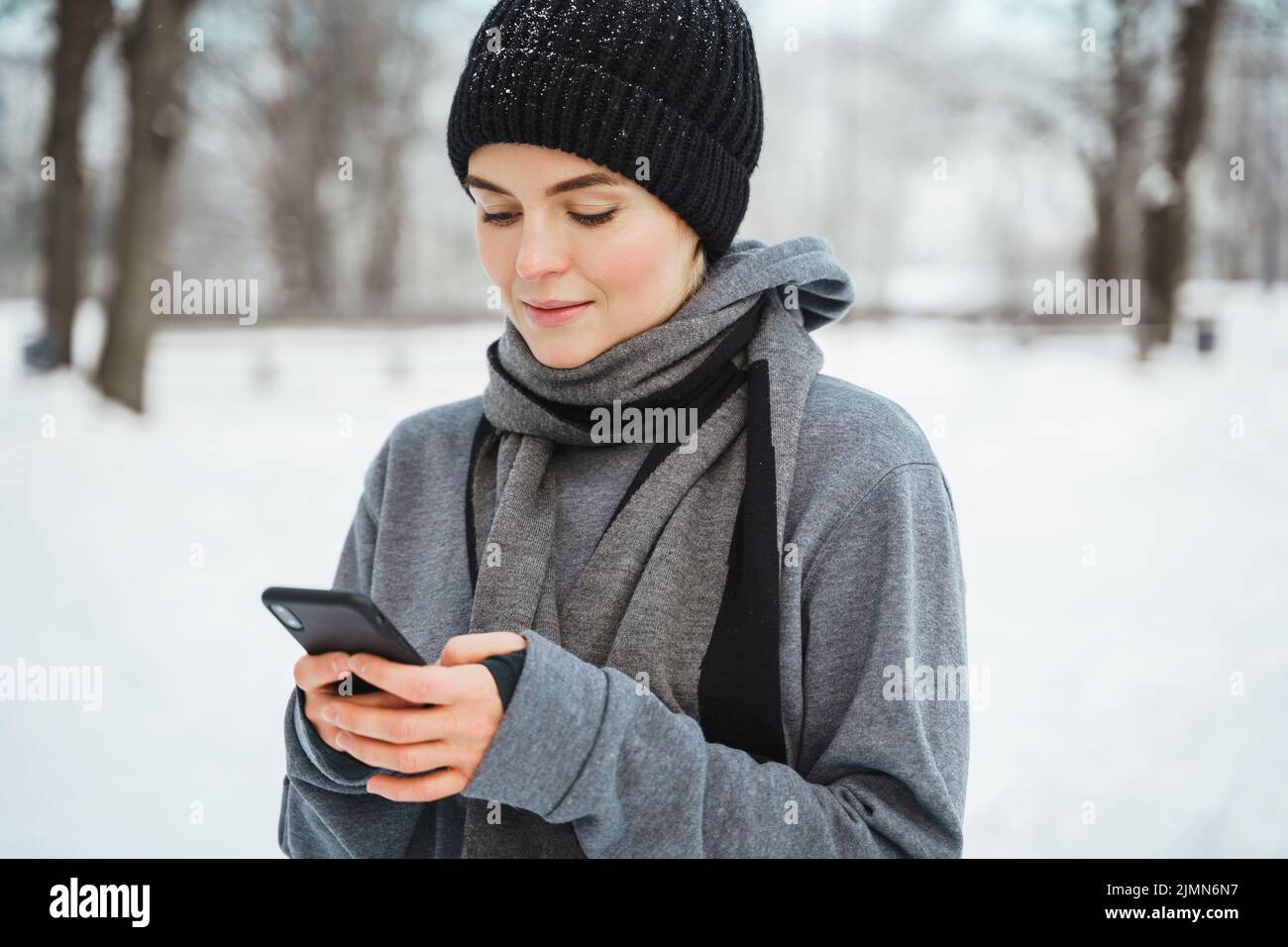 Donna atletica che usa lo smartphone durante il suo allenamento invernale nel parco innevato Foto Stock