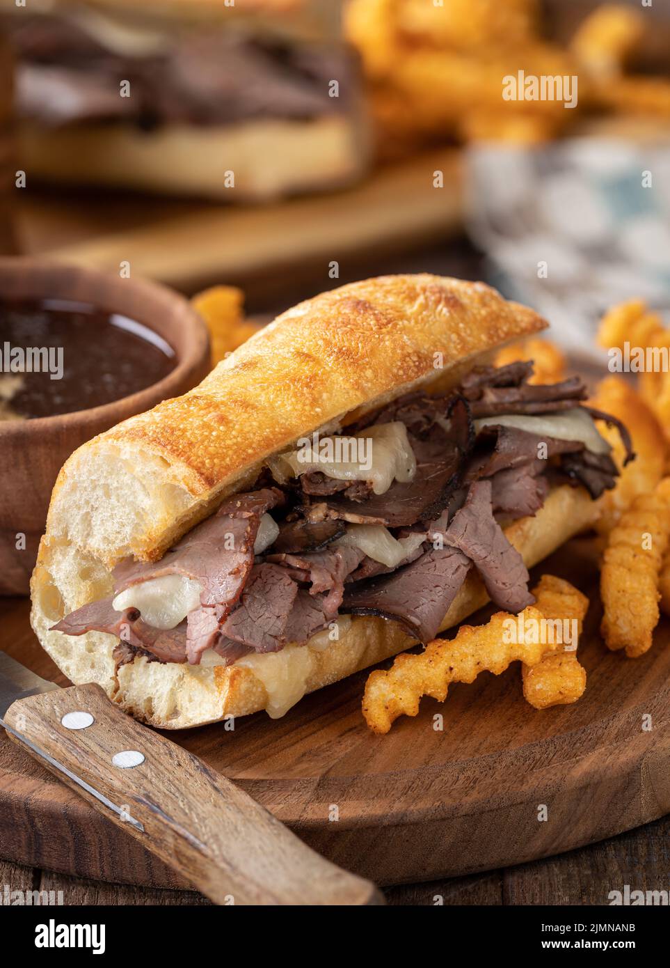 Sandwich con salsa francese e patatine fritte con ciotola di au jus sullo sfondo su un piatto di legno Foto Stock