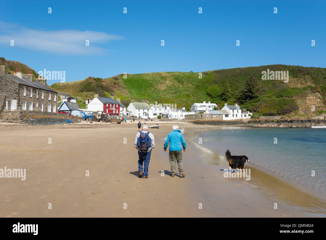 Coppia cane a piedi a Porthdinllaen vicino Morfa Nefyn sulla costa del Galles del Nord. Il ben noto Ty Coch Inn visto tra i cottage imbiancati. Foto Stock