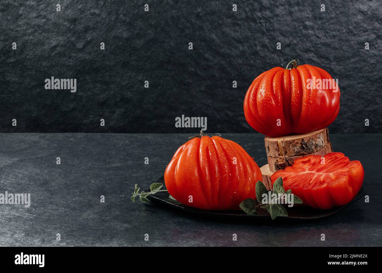 Un gruppo di grossi pomodori Costoluto con origano su sfondo grigio, spazio per il testo Foto Stock