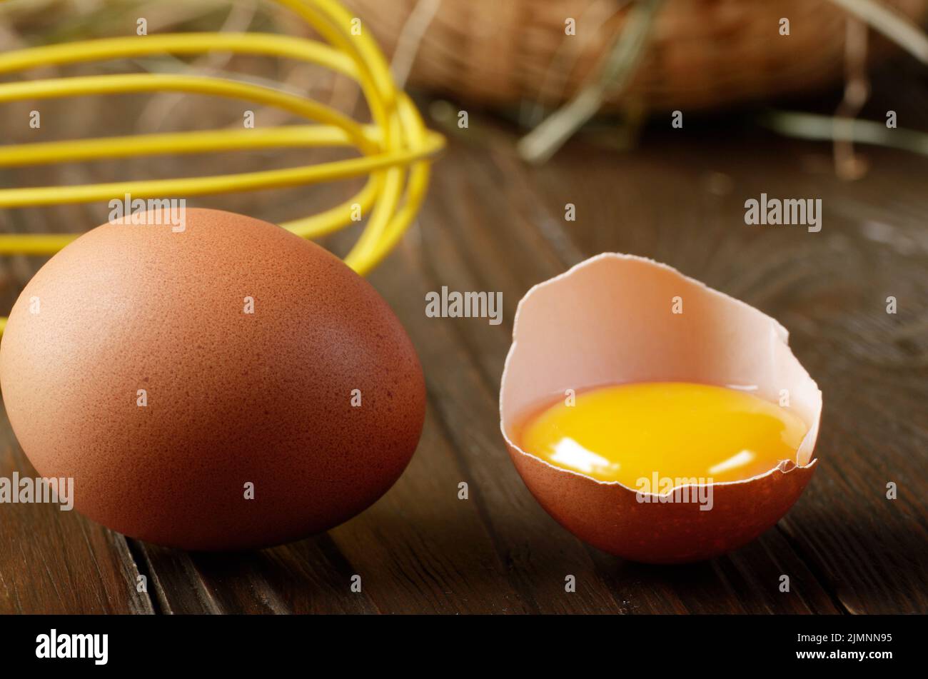 Materie organiche di pollo marrone uova rotte con tuorlo d'uovo cesto in vimini e una frusta su cucina tavolo in legno Foto Stock
