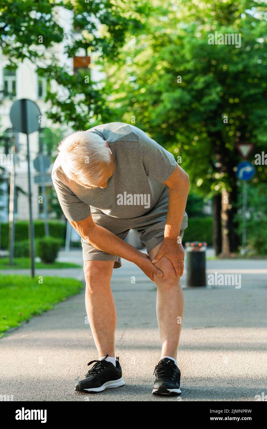 Uomo anziano che soffre di dolore al ginocchio durante il suo allenamento da jogging Foto Stock