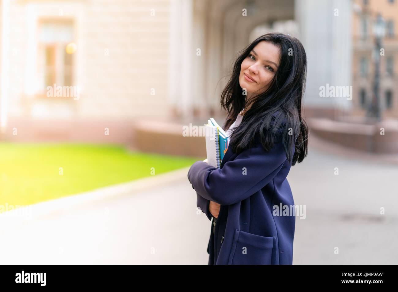 Bella ragazza sorridente bruna studente in possesso di notebook e libri di testo, si trova presso l'Università in strada di San Pietroburgo. Un cha Foto Stock