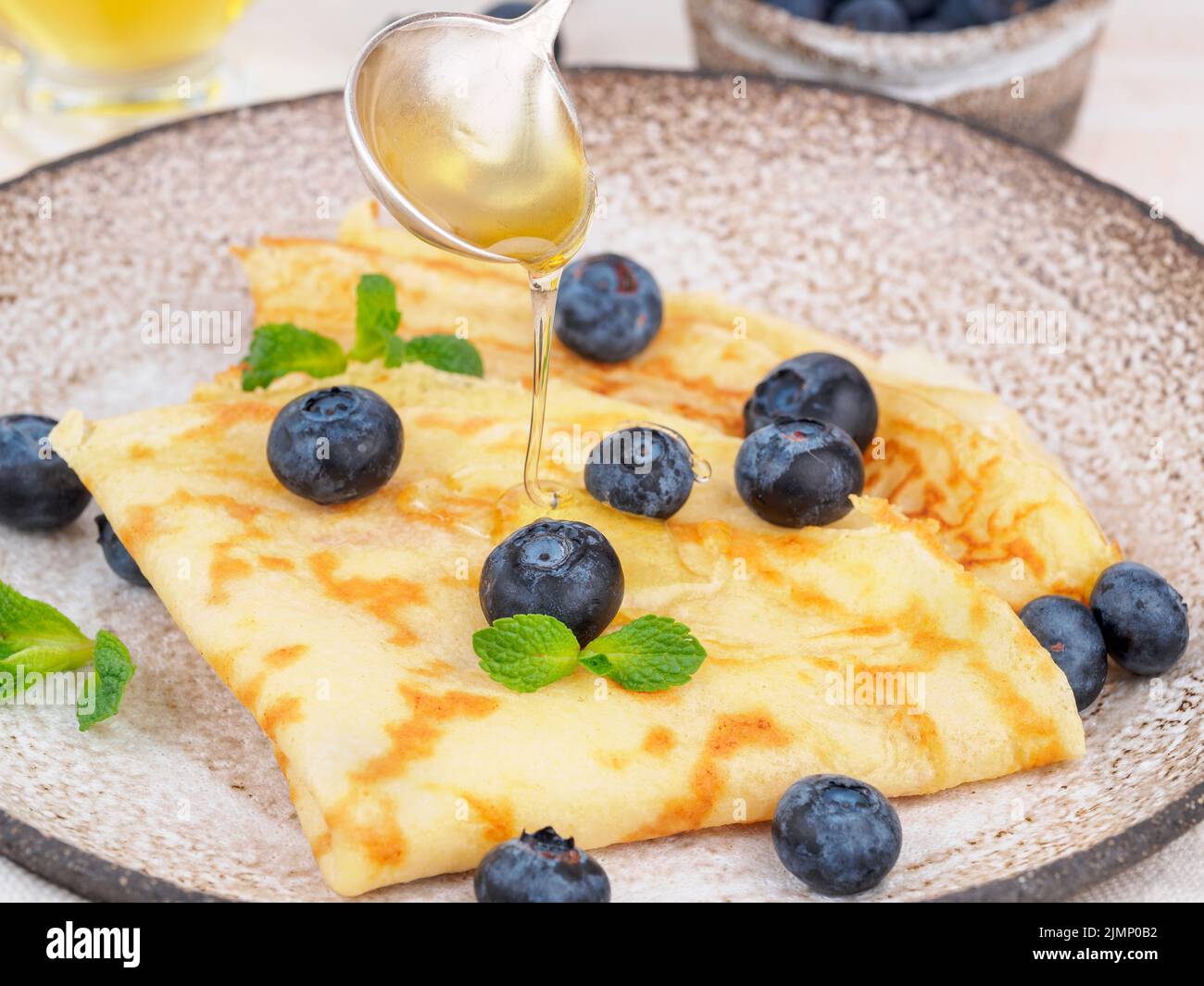 Due pancake con mirtilli e miele sul piatto, flussi di miele dal cucchiaio, vista laterale, primo piano Foto Stock