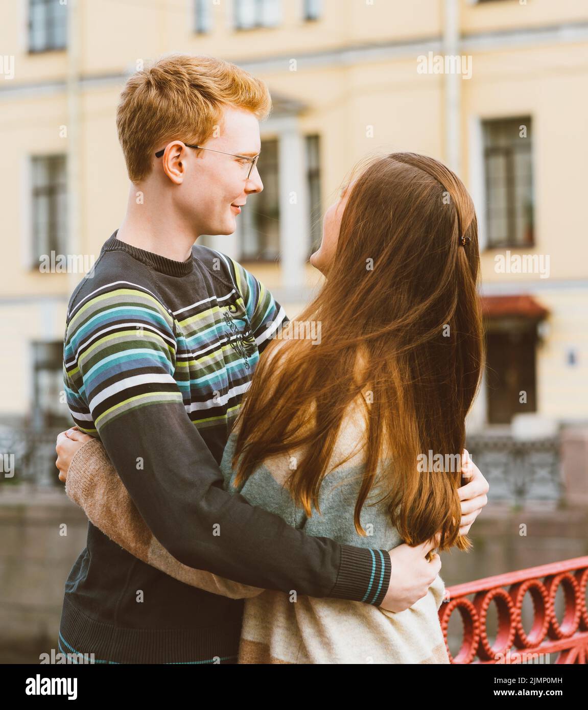 Ragazza con lungo spesso scuro sentire abbracciare il ragazzo rosso nella t-shirt blu su un ponte, giovane coppia. Concetto di amore adolescente e. Foto Stock