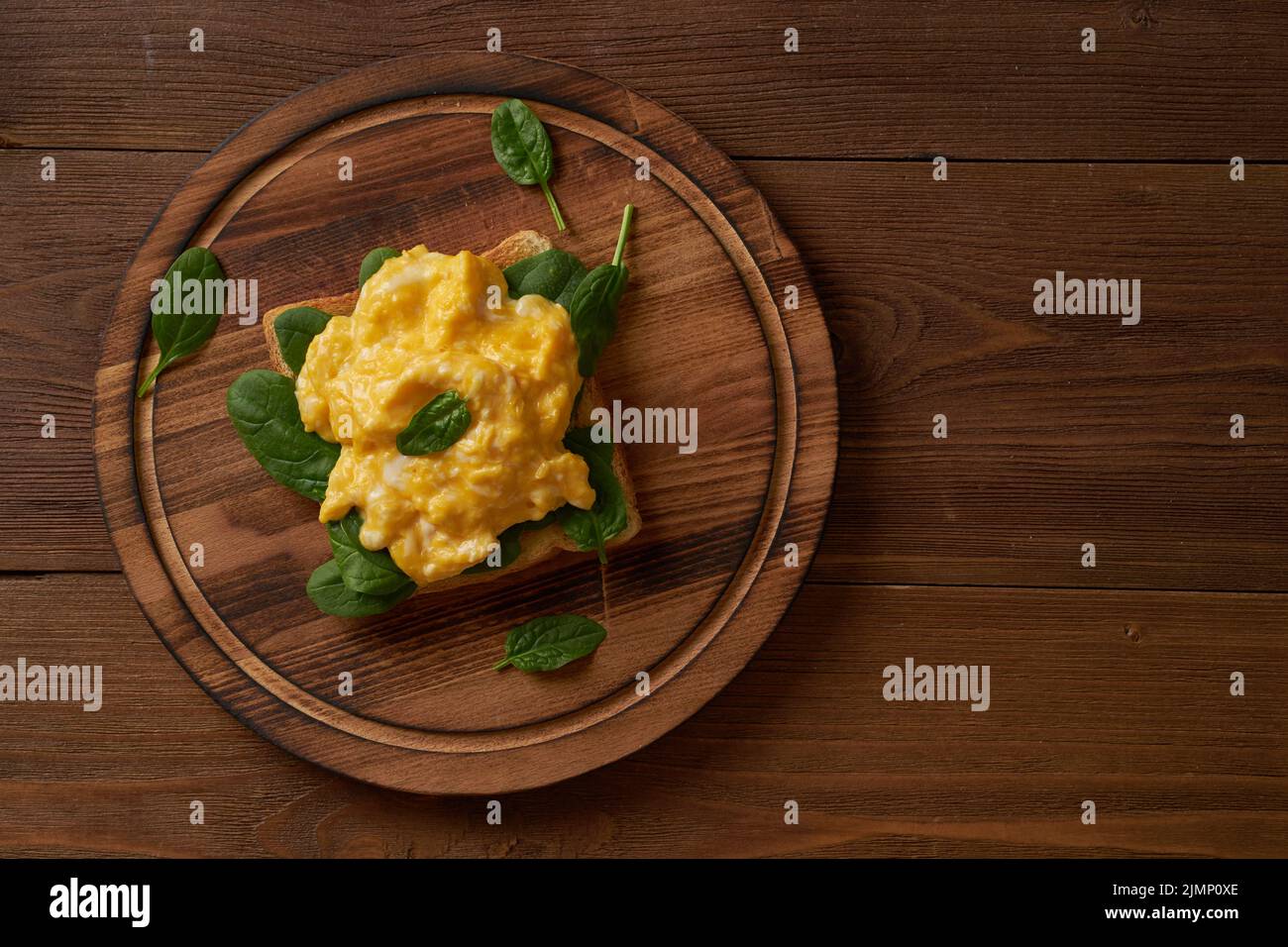 Toast con uova strapazzate e spinaci. Omelette. Prima colazione con uova fritte su sfondo marrone scuro. Vista dall'alto. Foto Stock