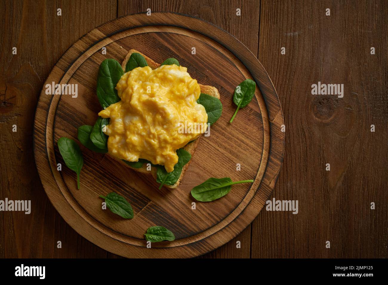 Toast con uova strapazzate e spinaci. Omelette. Prima colazione con uova fritte su sfondo marrone scuro. Vista dall'alto. Foto Stock