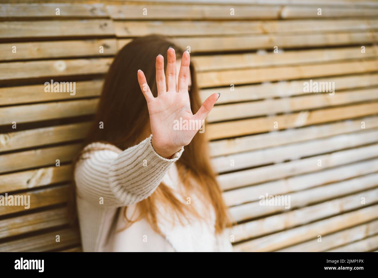 Donna con i capelli lunghi raggiunge in avanti, proteggendo il viso dalla fotocamera. Concetto di privacy, spazio personale, divieto di fotogr Foto Stock