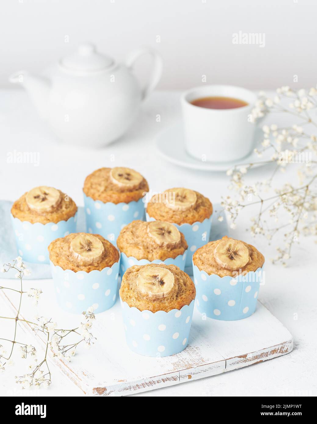 Muffin alla banana, cupcakes in cartine blu, vista laterale, verticale, tavolo bianco in cemento Foto Stock