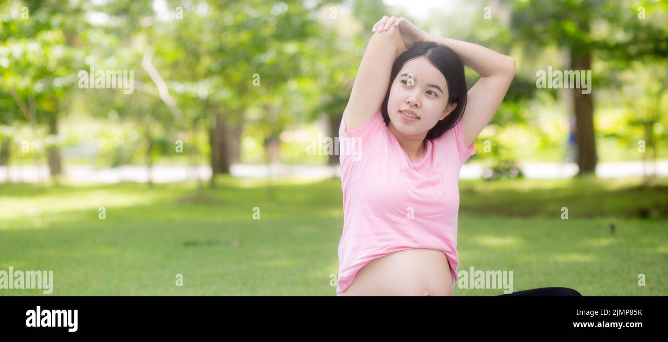 Felicità giovane donna asiatica incinta seduta facendo esercizio sportivo con mani stretch muscolo per la salute al parco, madre che pratica yoga per il leisur Foto Stock
