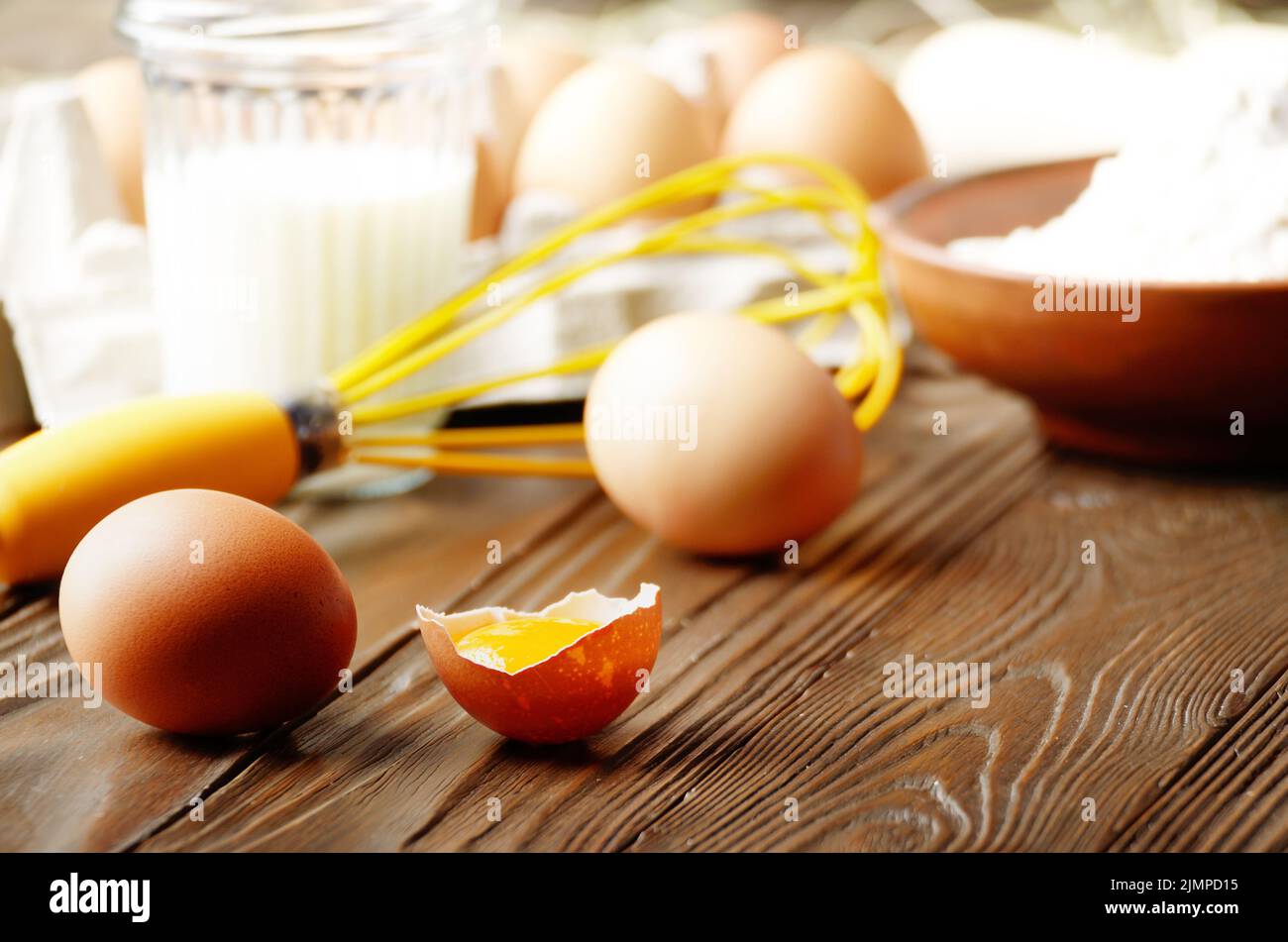 Materie organiche di pollo marrone uova rotte con tuorlo d'uovo farina latte e mescolare con una frusta da cucina tavolo in legno Foto Stock