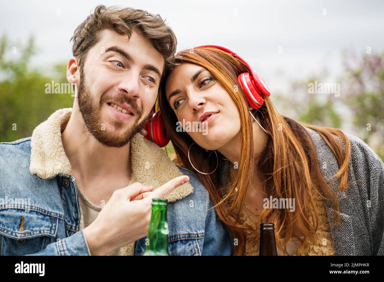 Due amici felici che condividono le cuffie per ascoltare la loro canzone preferita seduti insieme nel parco: People e Technology Concept Foto Stock