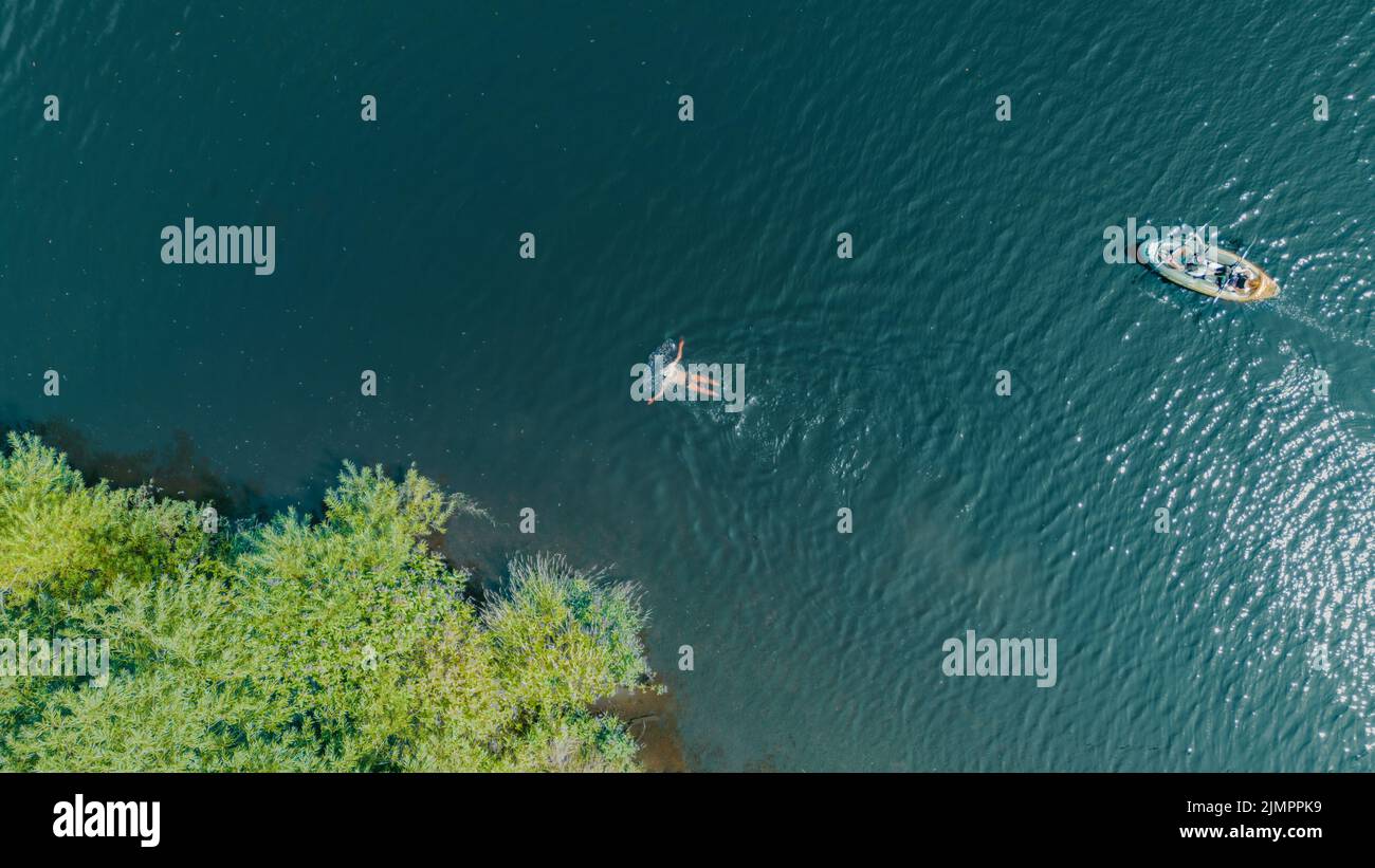 Vista aerea di un uomo che nuota in un fiume seguita da un paio di kayak in un kayak su acque turchesi. Drone shot uccelli vista occhio. Fiume Wharfe Foto Stock
