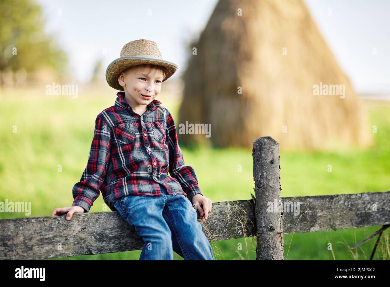 Primo piano ritratto di bambino in cappello seduto su recinto di legno Foto Stock