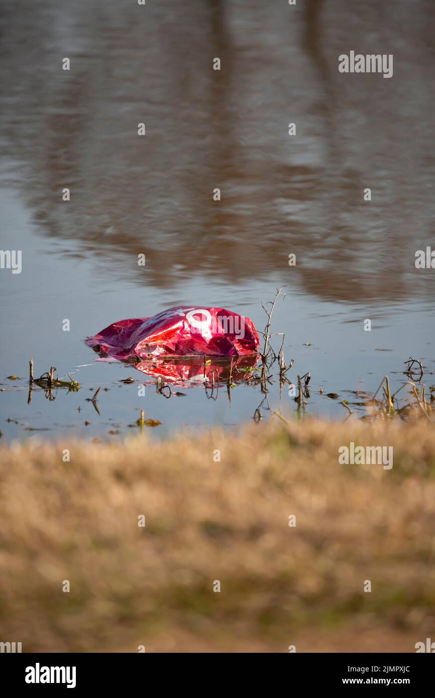 Palloncino in mylar rosso sgonfio galleggiante vicino al bordo dell'acqua Foto Stock