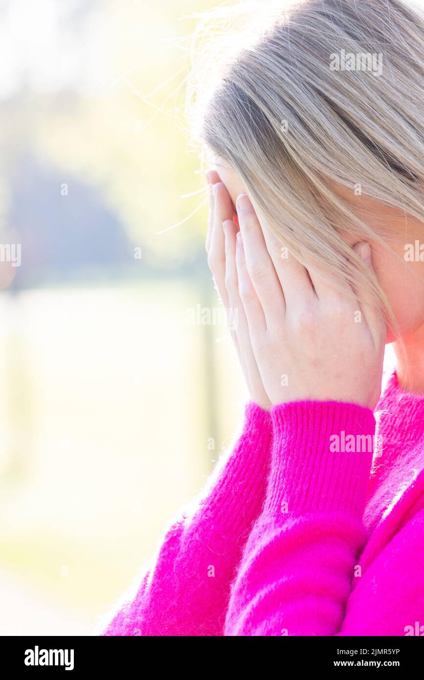 Triste stanco giovane bella donna bionda con il viso nelle sue mani spaventato, avendo ansia o mal di testa emicrania o depre Foto Stock