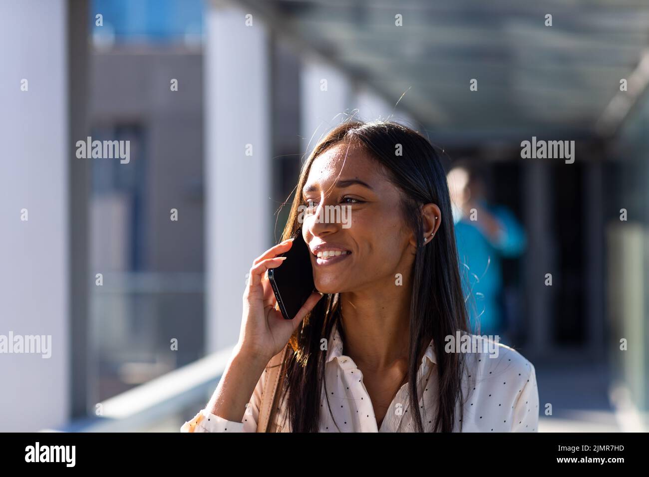 Sorridendo giovane donna d'affari biraciale che parla al telefono cellulare in corridoio sul posto di lavoro Foto Stock