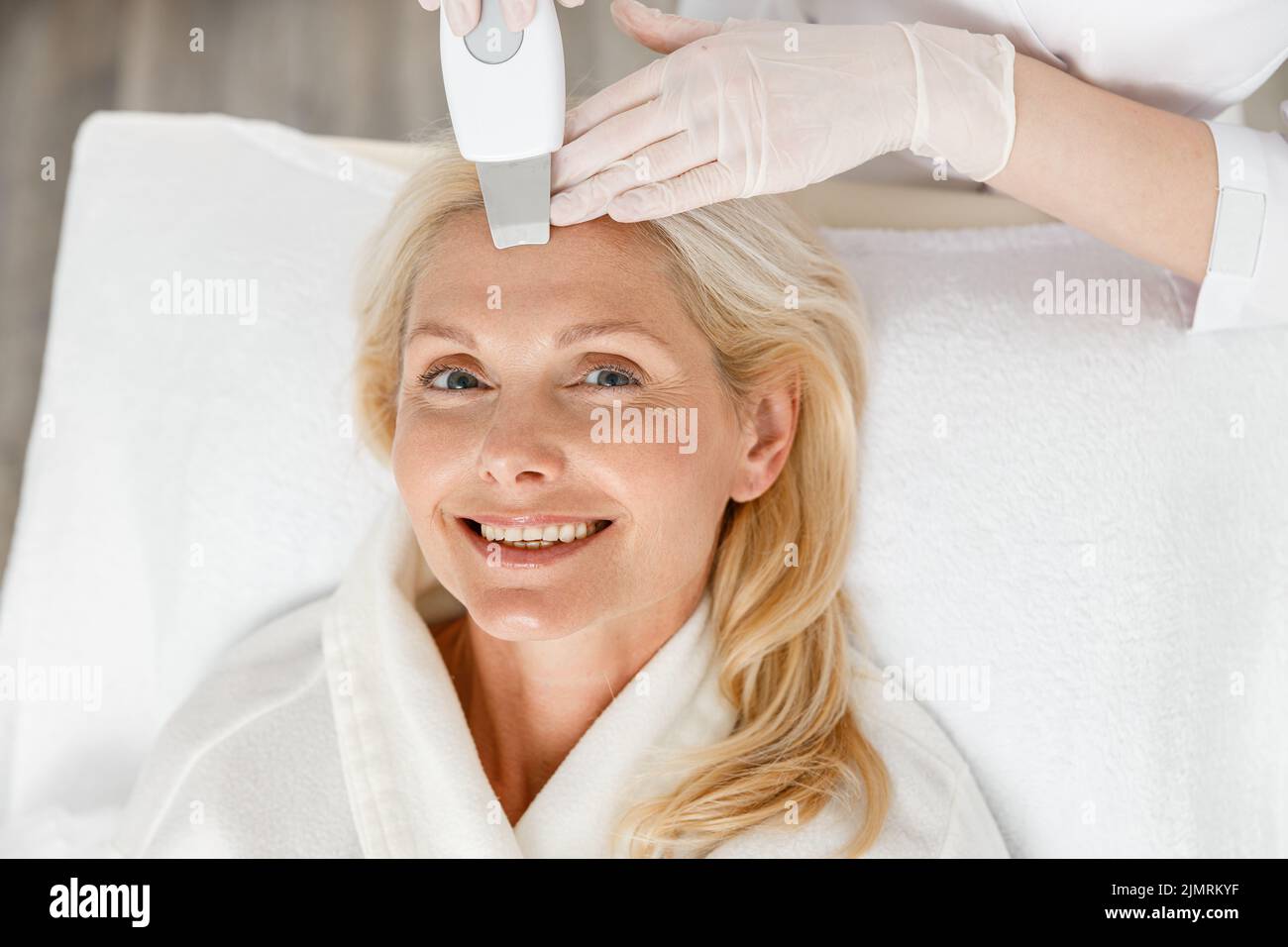 Estetician fare la pulizia ultrasonica del viso per la donna abbastanza felice di mezza età, primo piano Foto Stock