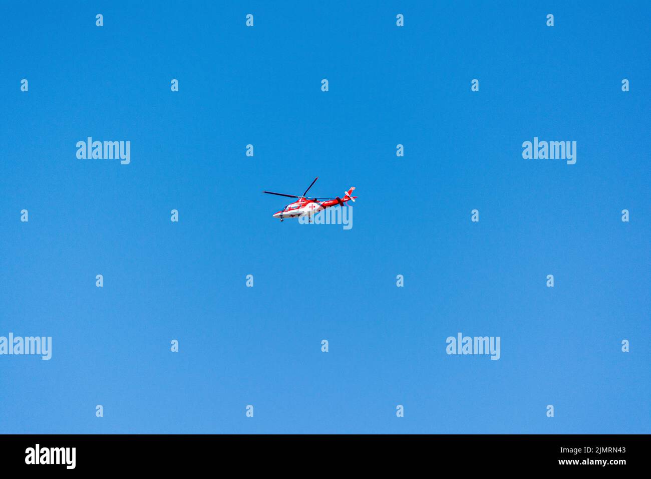 Un elicottero medico con una croce rossa che vola sullo sfondo blu del cielo Foto Stock