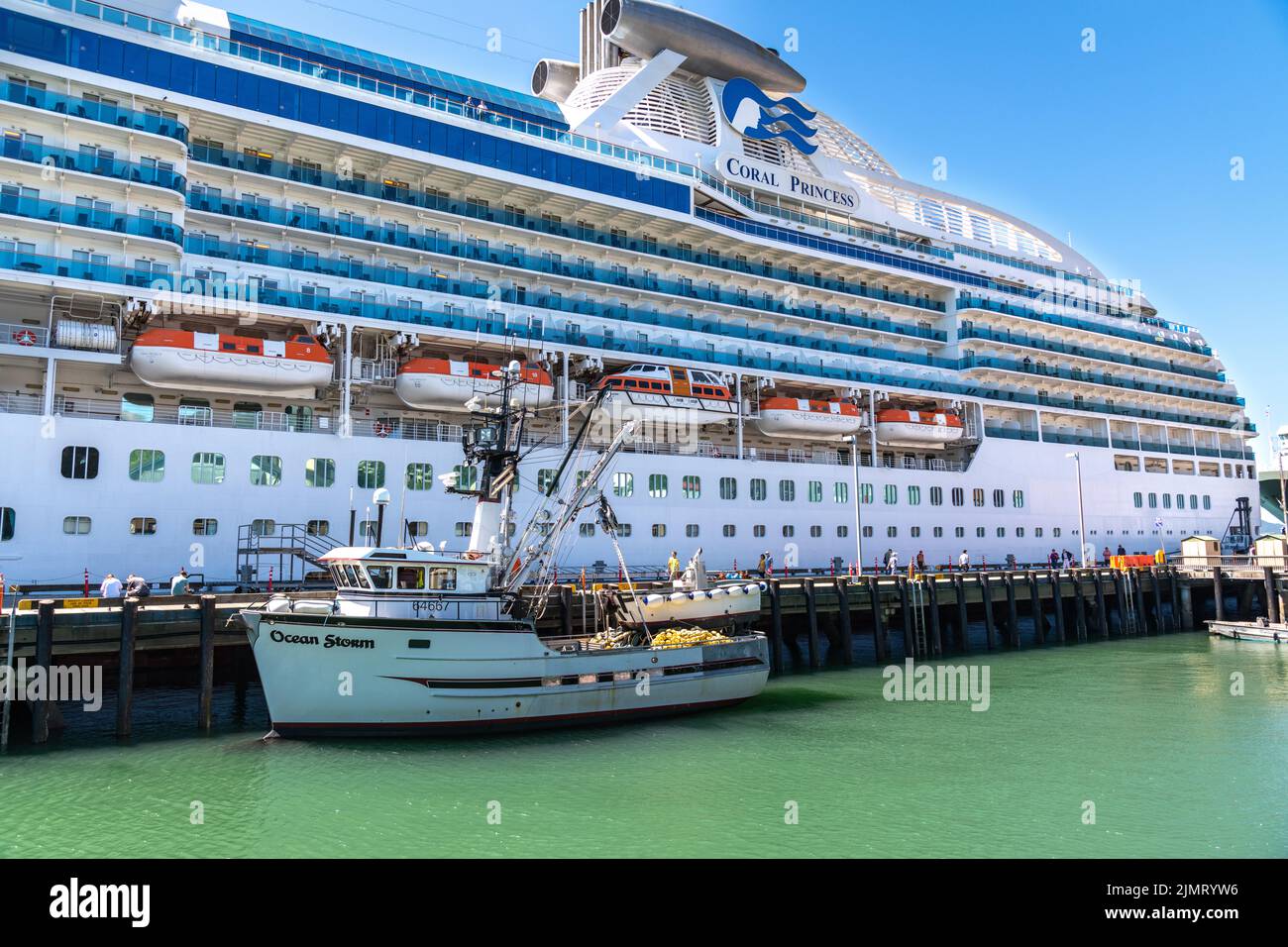 Una barca da pesca legata accanto alla gigantesca nave da crociera Coral Princess ai moli delle navi da crociera nel centro di Ketchikan, Alaska. Foto Stock