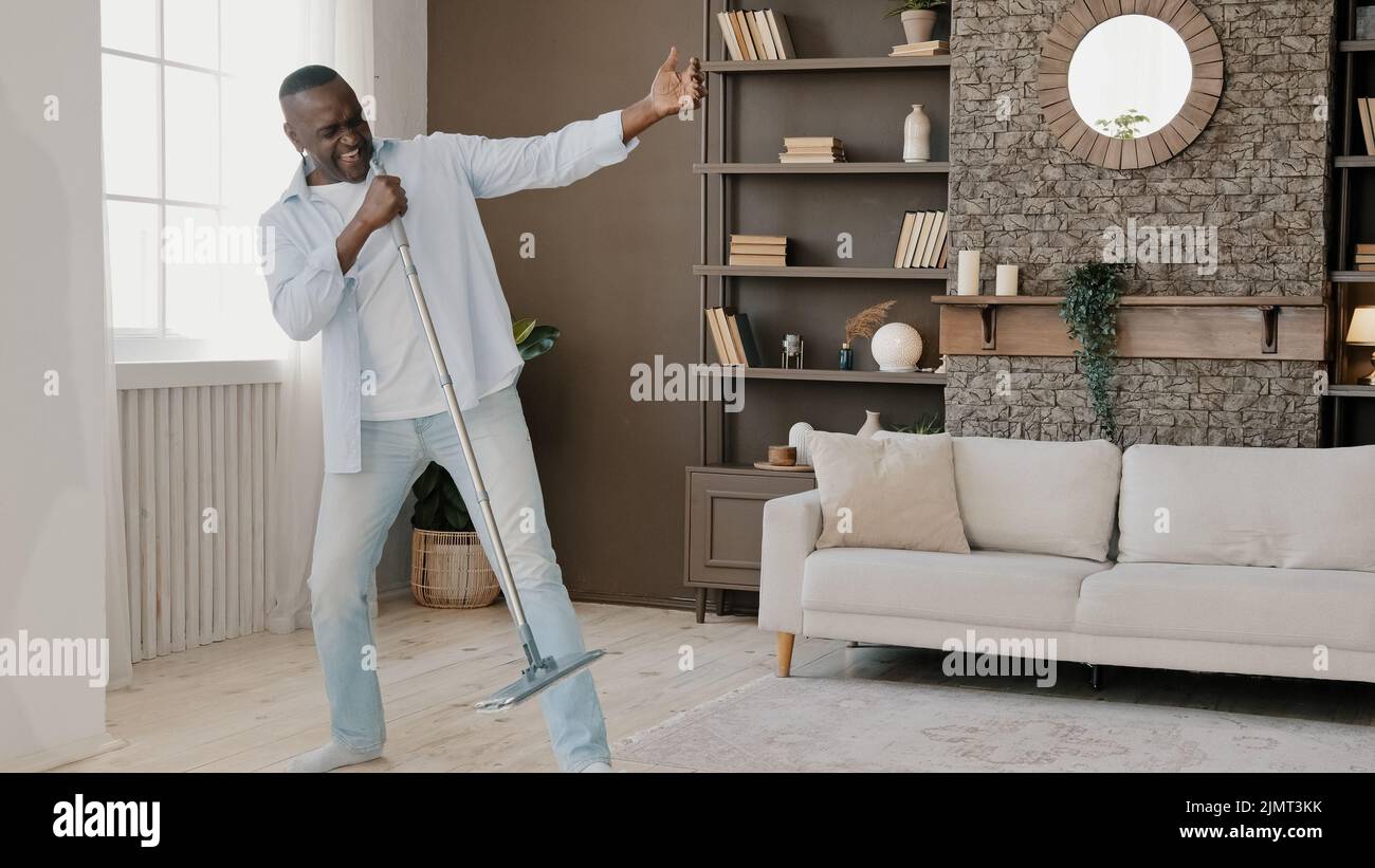 Maturo pazzo divertente afroamericano eccitato senior pensionato uomo lavaggio pavimento in casa appartamento danza attiva movimento per la musica ha divertimento facendo pulizia Foto Stock