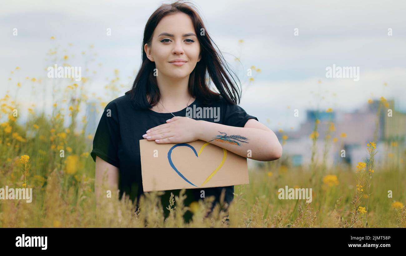 Attraente caucasico giovane ragazza donna patriota stand fuori tenere colorato cartone disegno amore forma cuore segno in ucraini colori blu Foto Stock