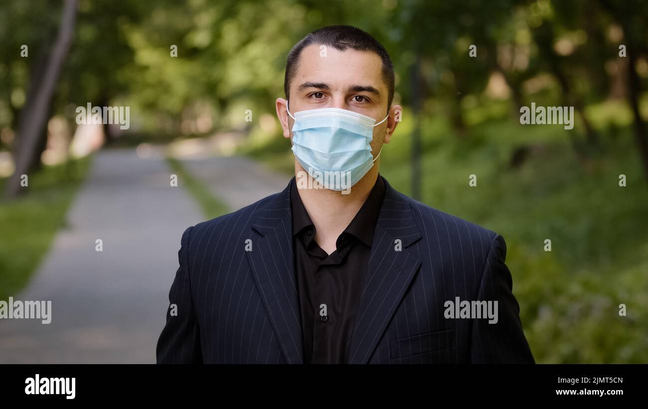 Uomo d'affari caucasico stanco toglie maschera medica respiratore protettivo uomo esausto si leva in piedi nel parco della città sente la libertà fa respiro profondo Foto Stock