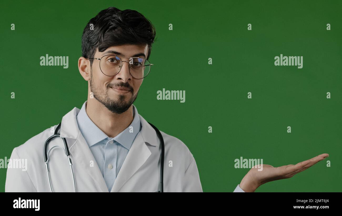 Arabo indiano ragazzo giovane maschio medico professionista uomo tenere spazio copia sulla palma puntando a spazio di lavoro mockup promo luogo per l'offerta di immagine della pubblicità Foto Stock