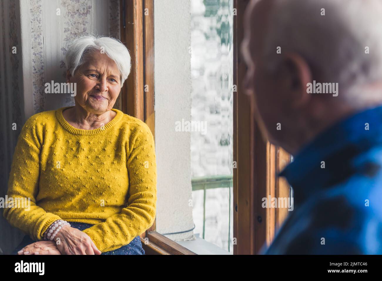 Gli anziani caucasici sposarono una coppia a casa seduta accanto alla finestra gelida e parlavano l'uno con l'altro. Foto di alta qualità Foto Stock