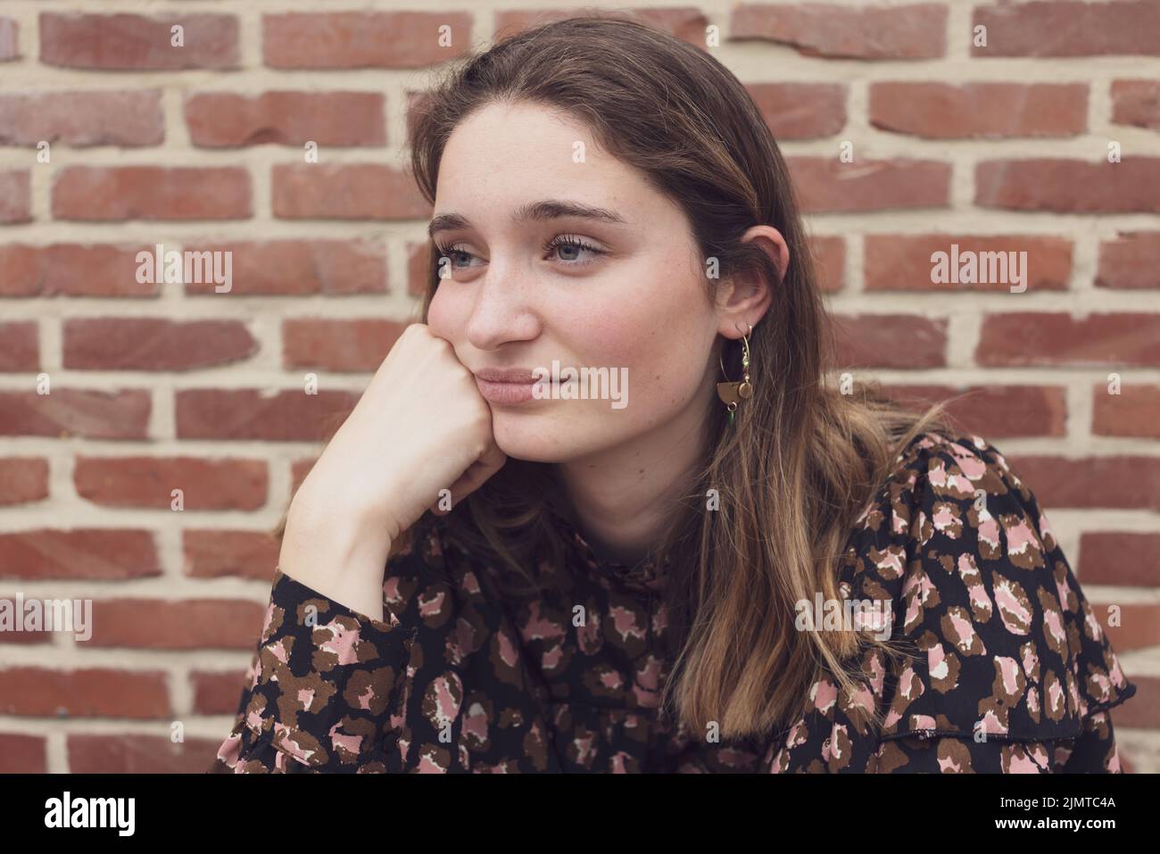 Primo piano ritratto di gioiosa 20s donna seduta da sola vicino al muro interno. Faccia di caucasica grave femmina con occhi tristi che fissano aw Foto Stock