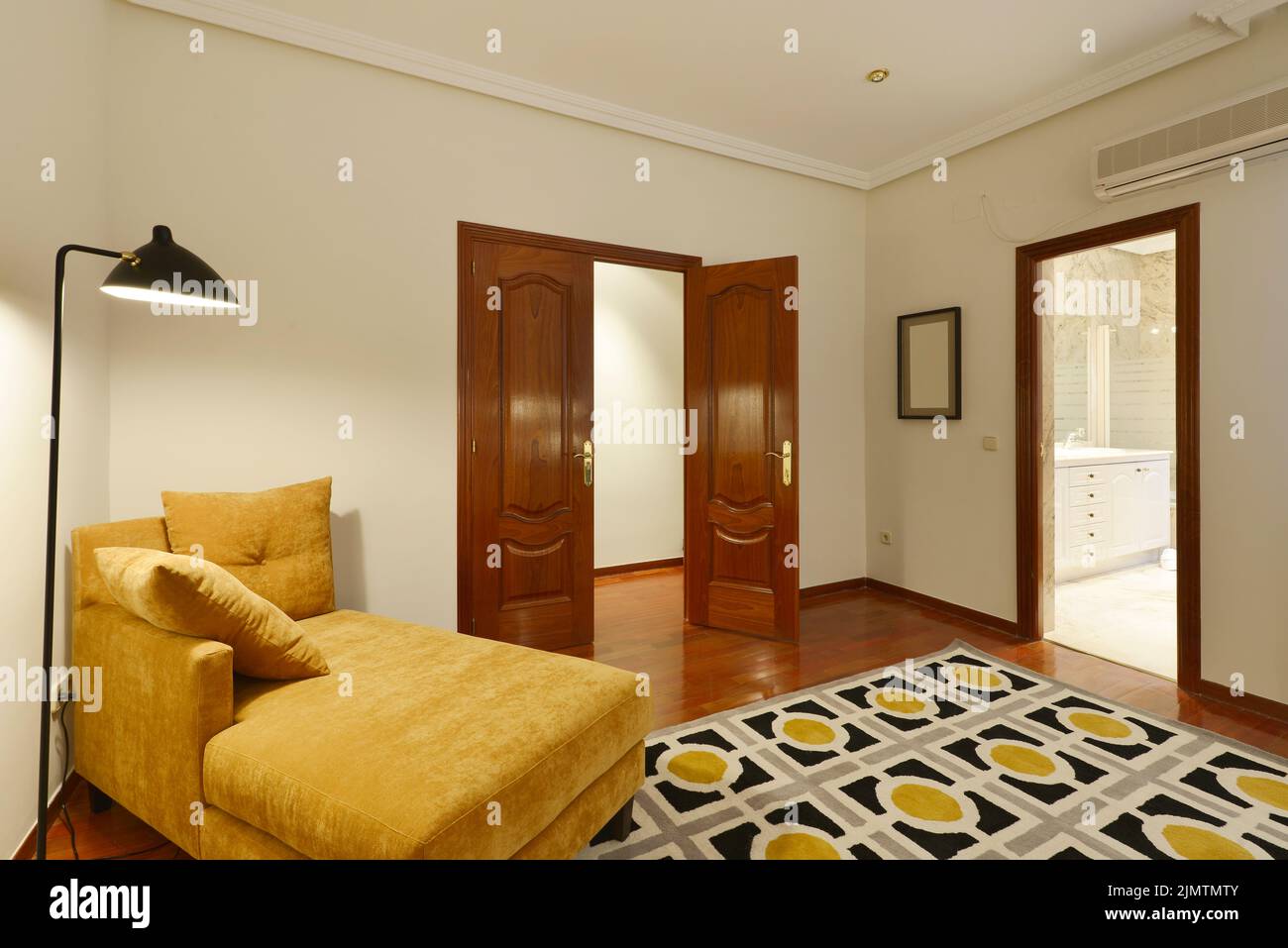 Angolo lettura in una camera da letto con moquette, pavimento in parquet rossastro e una chaise longue con cuscini in velluto cammello e una lampada di design nero, doppio ingresso Foto Stock