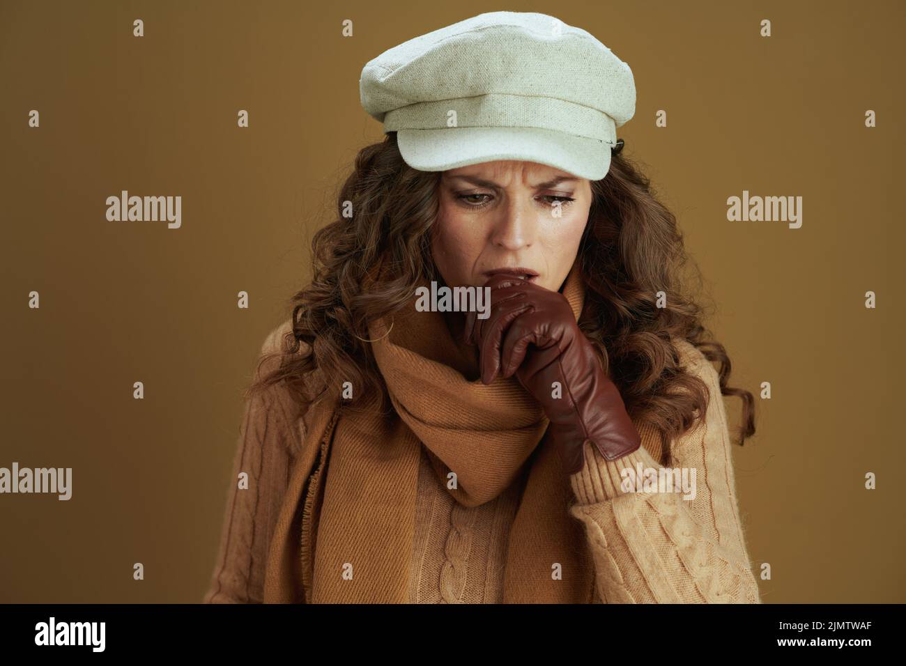 Ciao settembre. Elegante casalinga di mezza età in maglione con guanti di pelle tosse su sfondo di bronzo. Foto Stock
