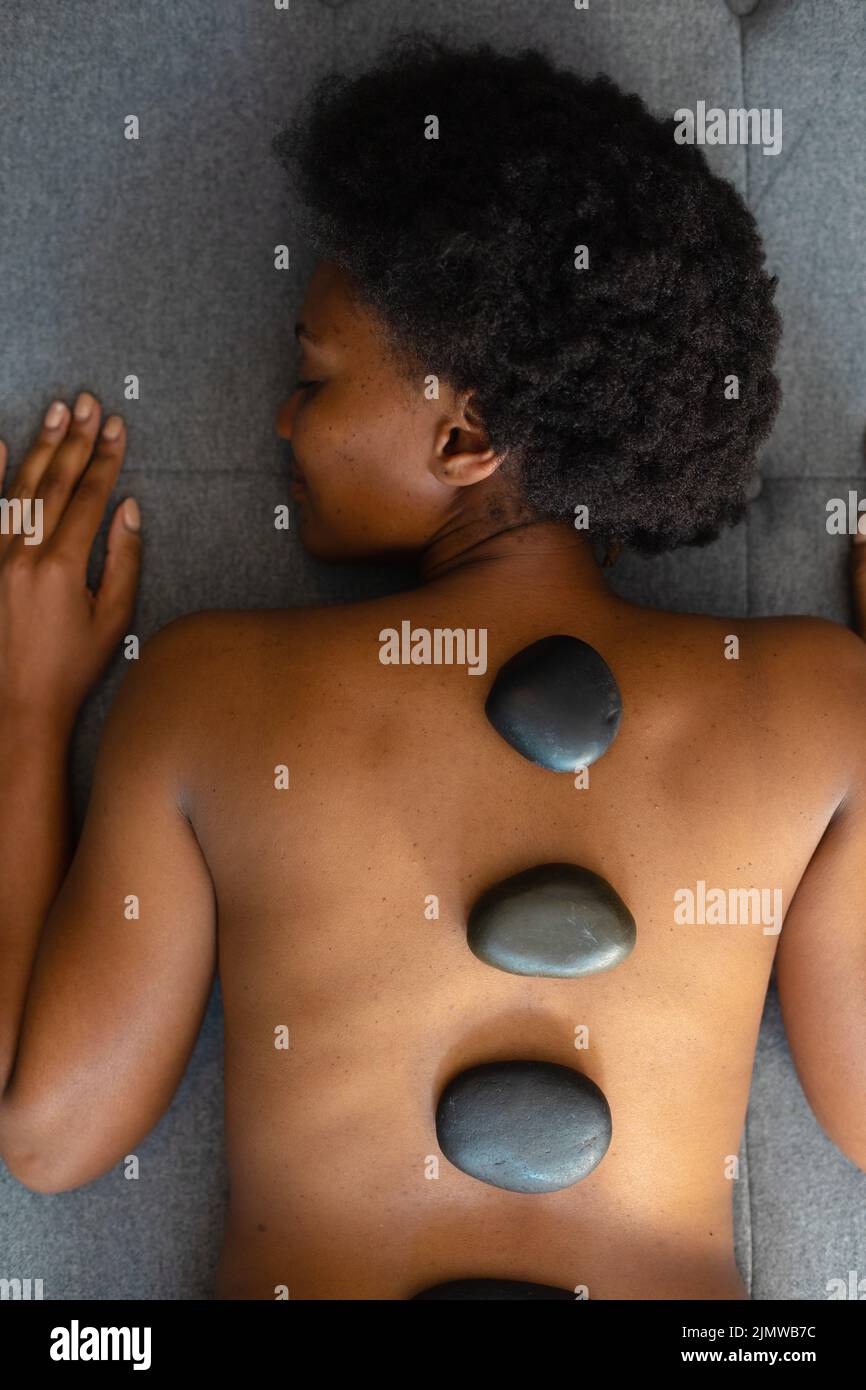Donna afroamericana con gli occhi chiusi ricevendo massaggio di pietra calda a casa. Concetto di spa, benessere e relax Foto Stock