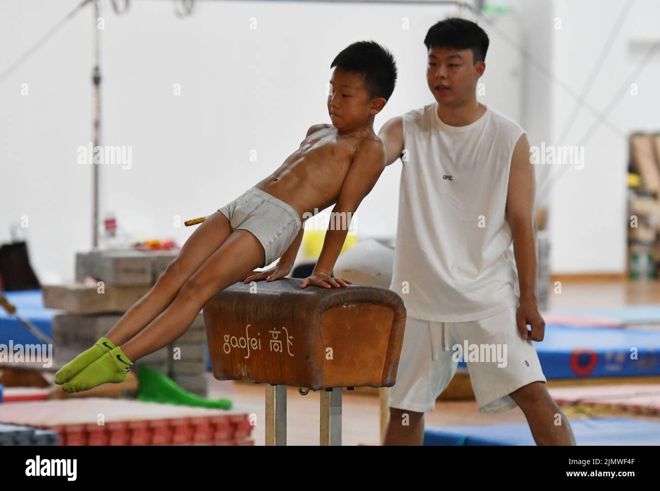 FUYANG, CINA - 7 AGOSTO 2022 - Un bambino pratica la ginnastica si muove sotto la guida di un allenatore alla palestra di Fuyang Vocational and Technical Foto Stock