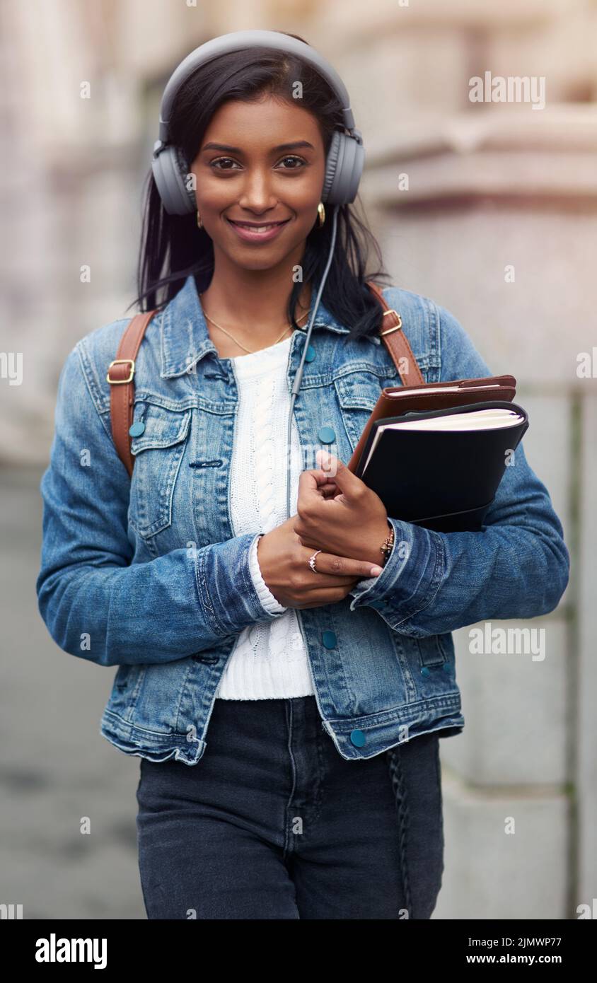 Il tuo futuro dipende da quello che fai oggi: Una giovane donna che cammina per la città indossando le cuffie mentre trasporta i suoi libri. Foto Stock